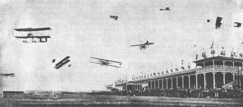 zobrazit detail historického snímku: Výjev z prvních aeronautických závodů v Remeši. — Současný let osmi aeroplanů.